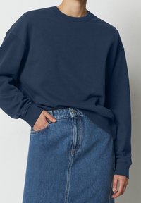 Sudadera azul marino de corte holgado, con cuello redondo acanalado y mangas largas, combinada con una falda de mezclilla de cintura alta que presenta una costura delantera.