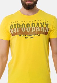 Gele katoenen T-shirt met een grafische print in zwart en bruin, met tekst die luidt "NY City Street Style" en "EST: 1996."