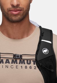 Zwarte hardloopvest met gaasaccenten, verstelbare banden en een sluiting. Beige shirt met een bedrukte logo, ronde halslijn en zichtbare stiksels.