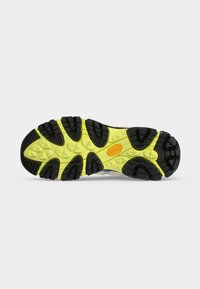 Semelle de chaussure avec motif de crampons noir et jaune et logo Vibram orange sur un fond gris clair uni.