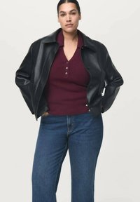 Veste en cuir noire avec col arrondi, pull boutonné bordeaux et jeans bleu à jambes larges. Texture lisse et design ajusté.