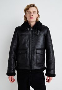 Black leather jacket with a shearling collar, front zipper, snap button pockets, and textured finish. Accented with buckle details on the collar.