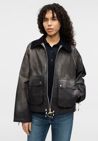 Αδιάβροχο μαύρο μπουφάν με φερμουάρ μπροστά, γιακά από κορντόρι, δύο μπροστινές τσέπες και λεπτομέρεια λογότυπου στην τσέπη. Ομαλή υφή.