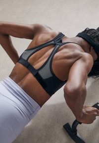 Black mesh sports bra with a racerback design, paired with light purple workout pants. Focus on athletic posture and grip on push-up handles.