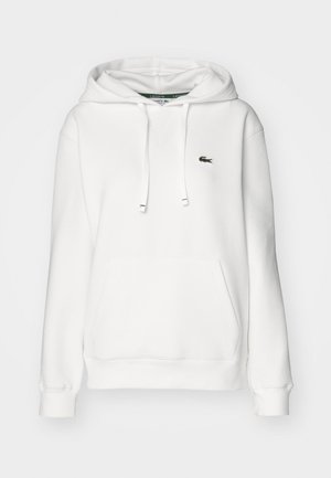 White hoodie with a kangaroo pocket, drawstring hood, ribbed cuffs, and a small green logo on the left chest. Soft fabric texture.