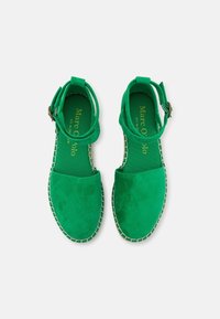 Gröna mockasandaler med platt sula, öppen tå, justerbart ankarsrem och vit sömnad längs kanterna. Texturerad innersula.