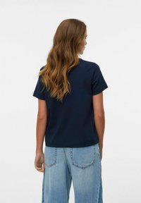 Mørkeblå, kortærmet t-shirt med lige snit og blødt stof, parret med lyseblå bukser med brede ben. Bagfra vises et simpelt design.