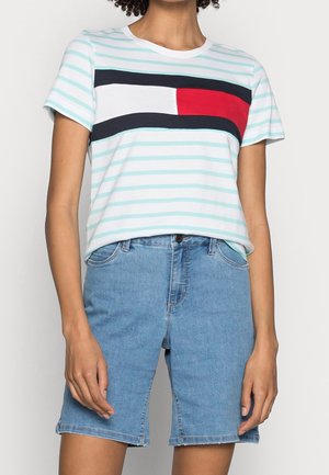 Jasnoniebieski bawełniany t-shirt w paski z krótkimi rękawami, z wyrazistym poziomym wzorem w kolorze białym, granatowym i czerwonym na klatce piersiowej. W zestawie z denimowymi szortami.