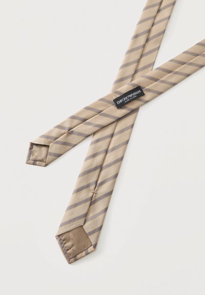 Cravate en soie beige à rayures grises diagonales, affichant l'étiquette Emporio Armani et des coutures détaillées sur un fond uni.
