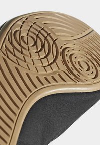 Black sneaker sole with a textured, rubber, circular, and wave pattern; beige edging highlights the design and enhances grip.