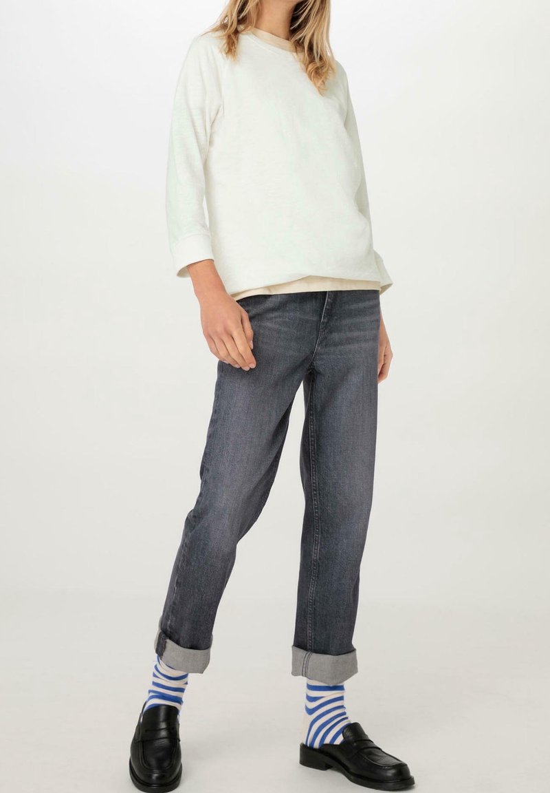 Light gray long-sleeve shirt layered over a cream top, paired with dark gray straight-leg jeans, rolled cuffs, and blue striped socks. Black loafers.