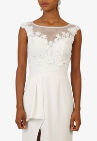 White dress featuring a floral lace bodice with a netted insert, a fitted waist, and a flowing pleated skirt with a side slit.
