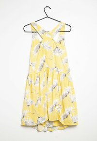 Gul blommig klänning med korsad ryggdesign, med vita och grå blommönster, samlad midja och en flödande kjol.