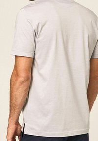 T-shirt gris à manches courtes avec un col rond. Il présente une coupe droite, des fentes latérales et un matériau en coton doux et lisse.