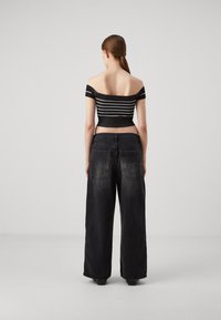 Top a righe bianche e nere senza spalline abbinato a jeans a gamba larga, neri sbiaditi, con tasche posteriori e dettaglio del logo del marchio.