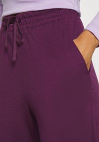 Lila joggingbyxor i mjukt material har en elastisk midja med dragsnöre och sidofickor för funktionalitet.