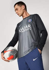 Dlhý rukáv čierny a šedý športový dres s vertikálnymi pruhmi, s logom "QATAR AIRWAYS" a emblémom PSG, skombinovaný s námorníckymi športovými nohavicami.