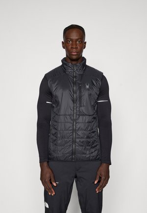 Mustapintainen eristettävä liivi, jossa on korkea kaulus, vetoketjulla suljettava etuosa, sivutaskut ja logoyksityiskohta. Rakenne on teksturoitu, mutta pinta on sileä.