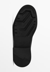 Semelle de chaussure noire présentant un motif texturé avec des rainures et des crêtes pour l'adhérence. Comprend un logo de marque et une finition lisse autour des bords.