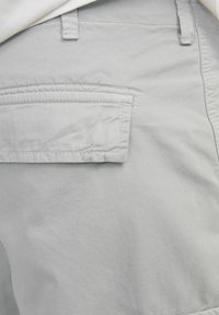 Shorts en tissu gris avec une poche arrière plate. Le matériau semble léger et légèrement texturé, avec des détails de couture visibles.
