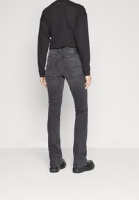 Camisa negra de manga larga combinada con jeans oscuros de corte ajustado. Los jeans cuentan con un diseño clásico de cinco bolsillos y un leve desgaste para dar textura.