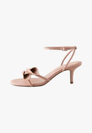 Blush pink open-toe sandal with mid-height thin heel, ankle strap with buckle, and floral detail on toe strap.