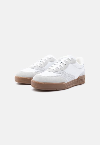 Λευκά χαμηλά αθλητικά παπούτσια με γκρι σουέντ λεπτομέρειες και καφέ λαστιχένιες σόλες, με λευκά κορδόνια και υφή στο πλάι.