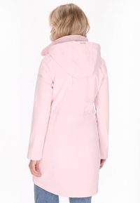 Rózsaszín vízhatlan kabát, kapucnival, hosszú ujjal és húzott derékkal. Sima textúra, látható minták vagy fém részek nélkül.