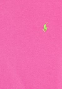 Bavlněné tričko v živé růžové barvě s malým zeleným vyšívaným logem polo hráče na levé hrudi. Hladká textura a kulatý výstřih.