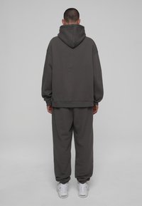 Overgrote grijze hoodie met kangoeroezak, gecombineerd met bijpassende sweatpants. Heeft geribbelde manchetten en zoom, zachte textuur, gedragen met witte sneakers.