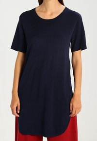 T-shirt blu navy a maniche corte con collo rotondo, realizzato in tessuto morbido, caratterizzato da una vestibilità rilassata e un orlo arrotondato, indossato con pantaloni rossi.