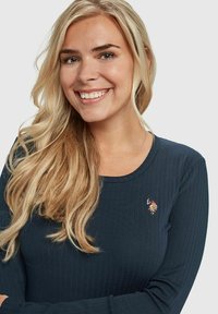 Navy ribbestrøye med lange ermer, rund hals og brodert logo på brystet. Myk tekstur, tettsittende design.