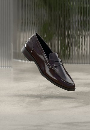 Mocassins en cuir marron à finition brillante, avec une couture surélevée et un petit détail découpé à l'avant, ainsi qu'une semelle basse noire.