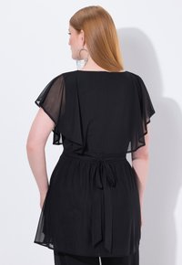 Top nero realizzato in tessuto leggero, con maniche a sbuffo trasparenti e un nastro in vita, progettato con una silhouette fluida.