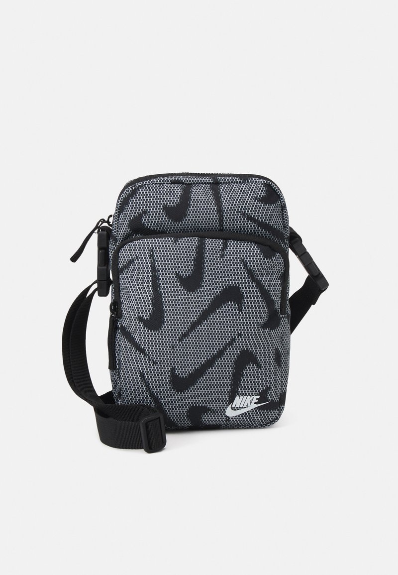 Černá a šedá ramenní taška Nike má síťovitou texturu, diagonální vzor s logem, horní zip a nastavitelný popruh. Kompaktní design pro snadné nošení.