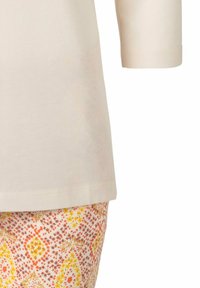 Helles beige Kurzarmoberteil kombiniert mit gemusterten Hosen, die orange, gelb und braune Blumenmuster auf einem cremefarbenen Hintergrund aufweisen.