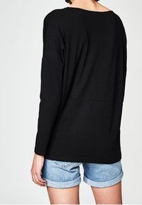 Svart långärmad topp med bred halsringning och avslappnad passform, kombinerad med ljusblå uppvikta denimshorts. Mjukt tyg med en minimal sömdetalj.