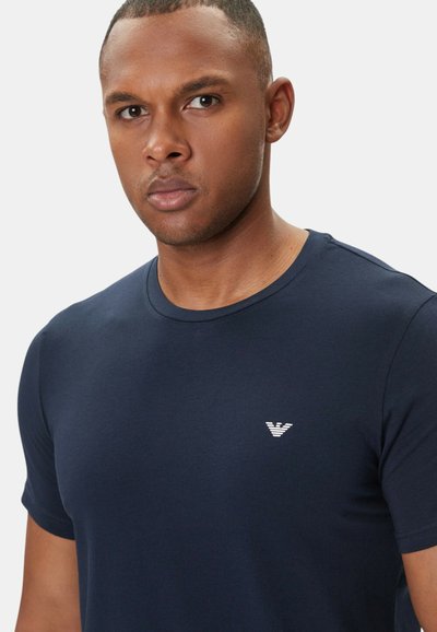 Laivastonsininen lyhythihainen T-paita, joka on valmistettu sileästä puuvillakankaasta. Tässä paidassa on pieni valkoinen logo rinnassa ja klassinen pyöreä kaula-aukko.