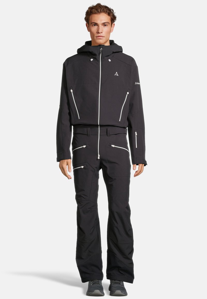 Giacca nera impermeabile con cappuccio regolabile e tasche con zip. Abbinata a pantaloni neri coordinati con dettagli con zip e una vestibilità slim.