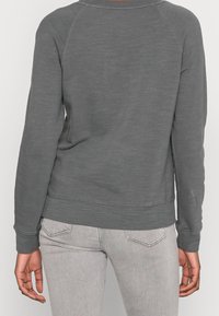 Sudadera de algodón gris con puños y dobladillo de canalé, que presenta un acabado texturizado. La vista trasera muestra mangas raglán y un diseño sencillo.