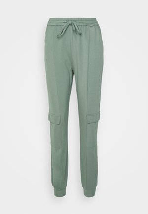 Calças de treino verdes feitas de um tecido suave, com uma cintura elástica ajustável, dois bolsos laterais e punhos ajustados. Projetadas com um detalhe de estilo cargo.