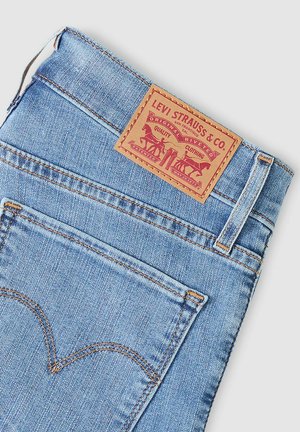 Siniset farkut, joissa on nahkainen merkkilappu kohokuvioiduilla kuvioilla, kontrastinompeleet ja klassinen taskumalli.