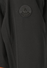 Schwarze Outdoor-Shorts aus strapazierfähigem Material, mit einer strukturierten Oberfläche und einem runden schwarzen Logo-Patch mit Bergdesign an der Seite.