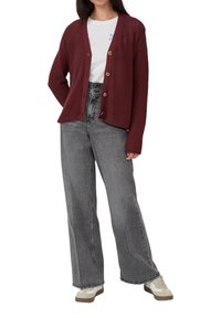 Cárdigan de punto burdeos con cinco botones de madera, combinado con jeans grises de pernera ancha de alta cintura y zapatillas beige.