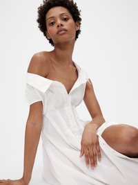 Hvit off-the-shoulder kjole med korte ermer, knapp-front design, rett snitt og myk tekstur, aksentuert med subtile draperinger.