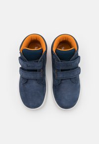 Adidași din suede bleu închis, cu talpă din cauciuc alb, dotati cu două curele velcro și un guler căptușit portocalie pentru confort.