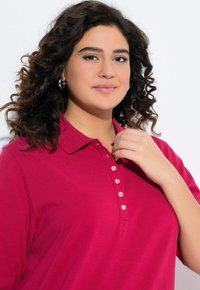 Polo shirt color lampone con colletto, dotato di una patta con sei bottoni beige e maniche corte. Tessuto in cotone liscio.