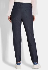 Donkergrijze, taps toelopende broek met een gladde textuur, voorzien van twee achterzakken en een elastische tailleband, gecombineerd met witte sneakers.