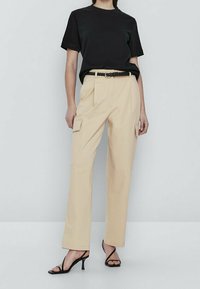 Zwart kortemouwen t-shirt gecombineerd met beige cargobroek met zijzakken en een gevlochten zwarte riem. Gestyled met zwarte hoge hakken sandalen.