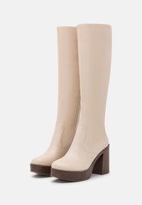 Knee-high beige leather boots with a smooth texture, square toe, and a wooden block heel. Features minimal stitching and side zipper detail.